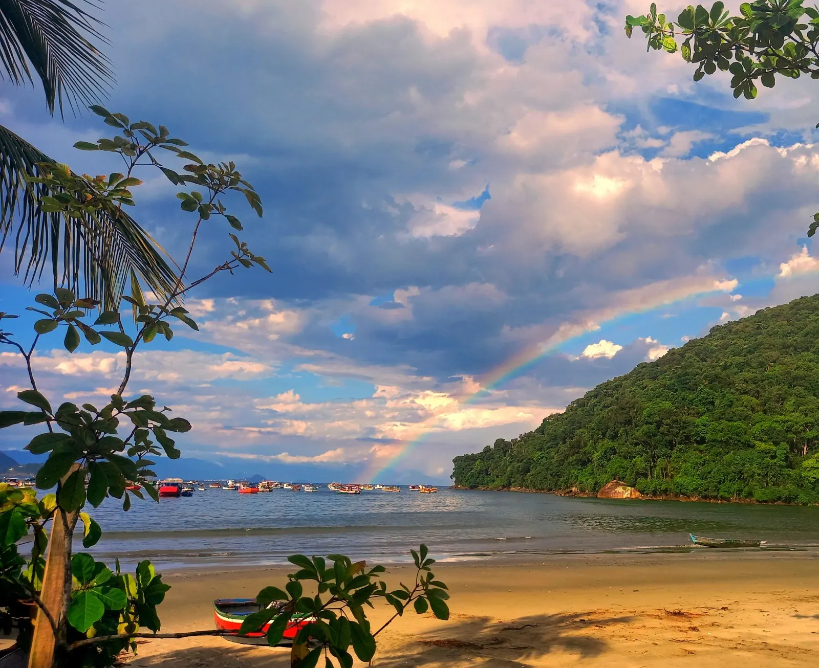 Praia em Guarujá com mar calmo, barcos e morro verde ao fundo